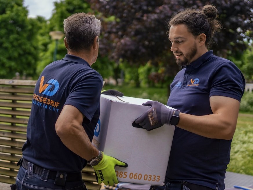 Twee verhuizers van Verhuisbedrijf Draagkracht dragen een verhuiskrat naar de wagen